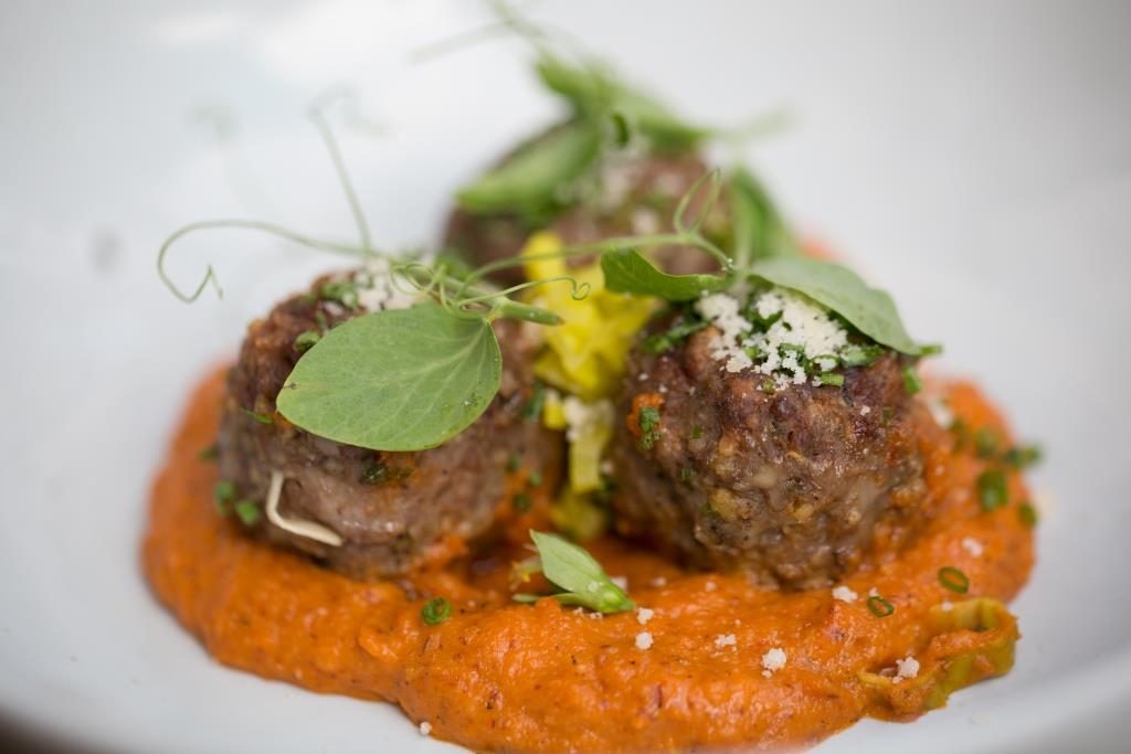 Lamb Meatballs on a pile of romesco sauce garnished with pea tendrils. 