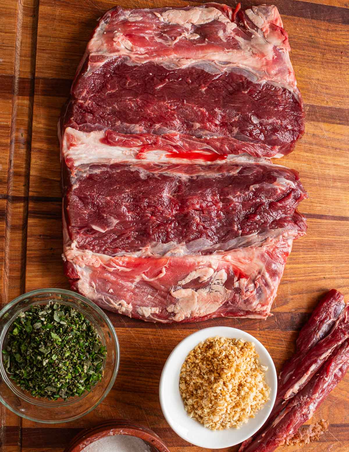 A deboned lamb saddle showing breadcrumbs, herbs and tenderloins on a cutting board.