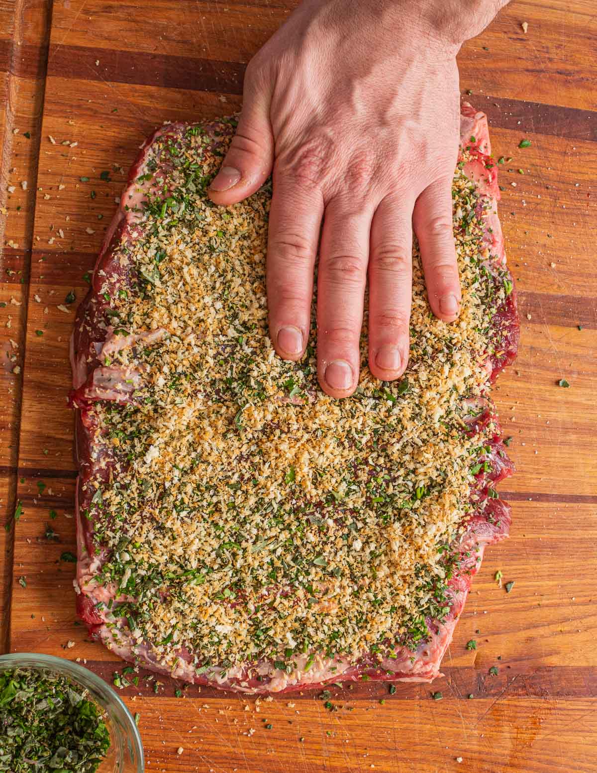 A hand pressing down breadcrumbs on a lamb saddle.