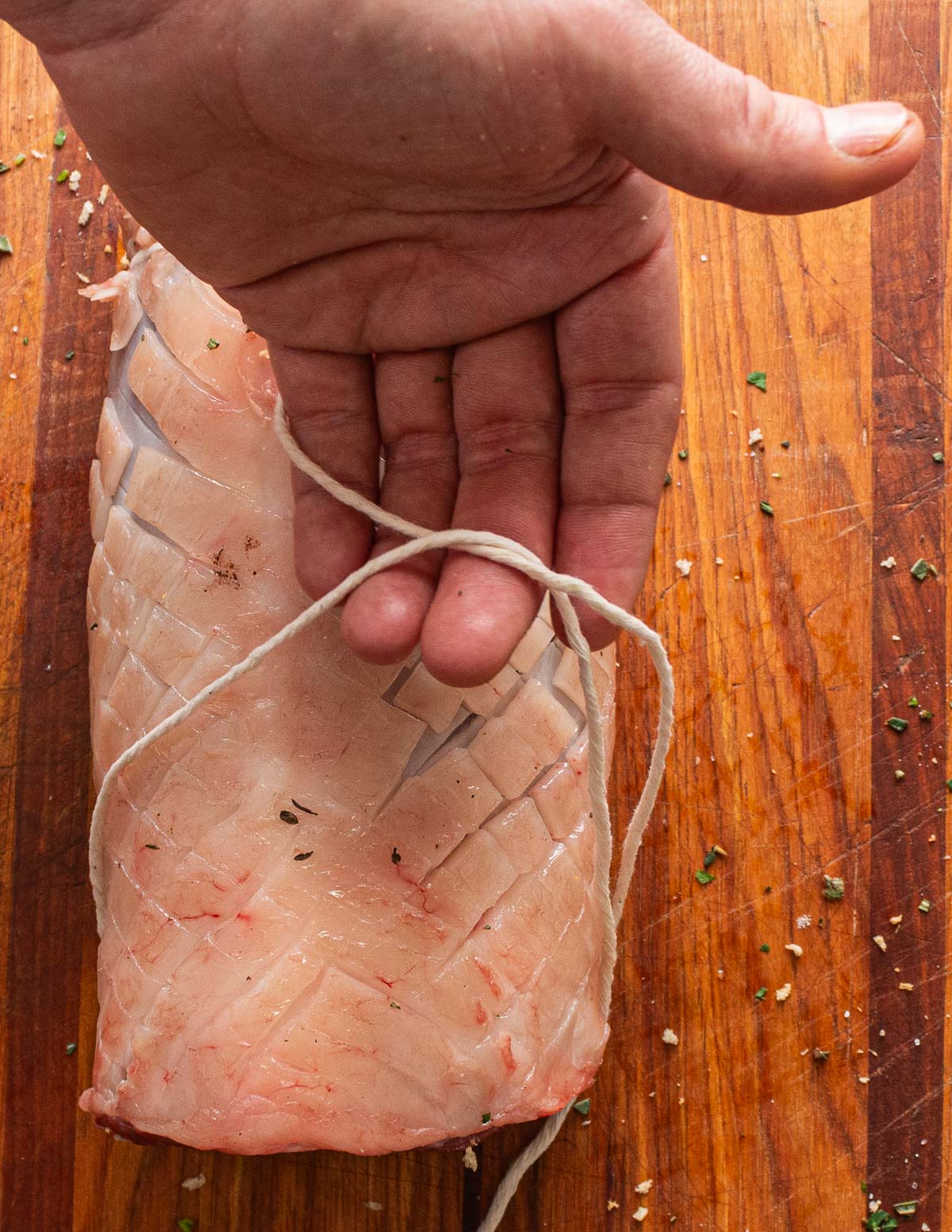 A hand tying a rolled lamb saddle with butchers twine.