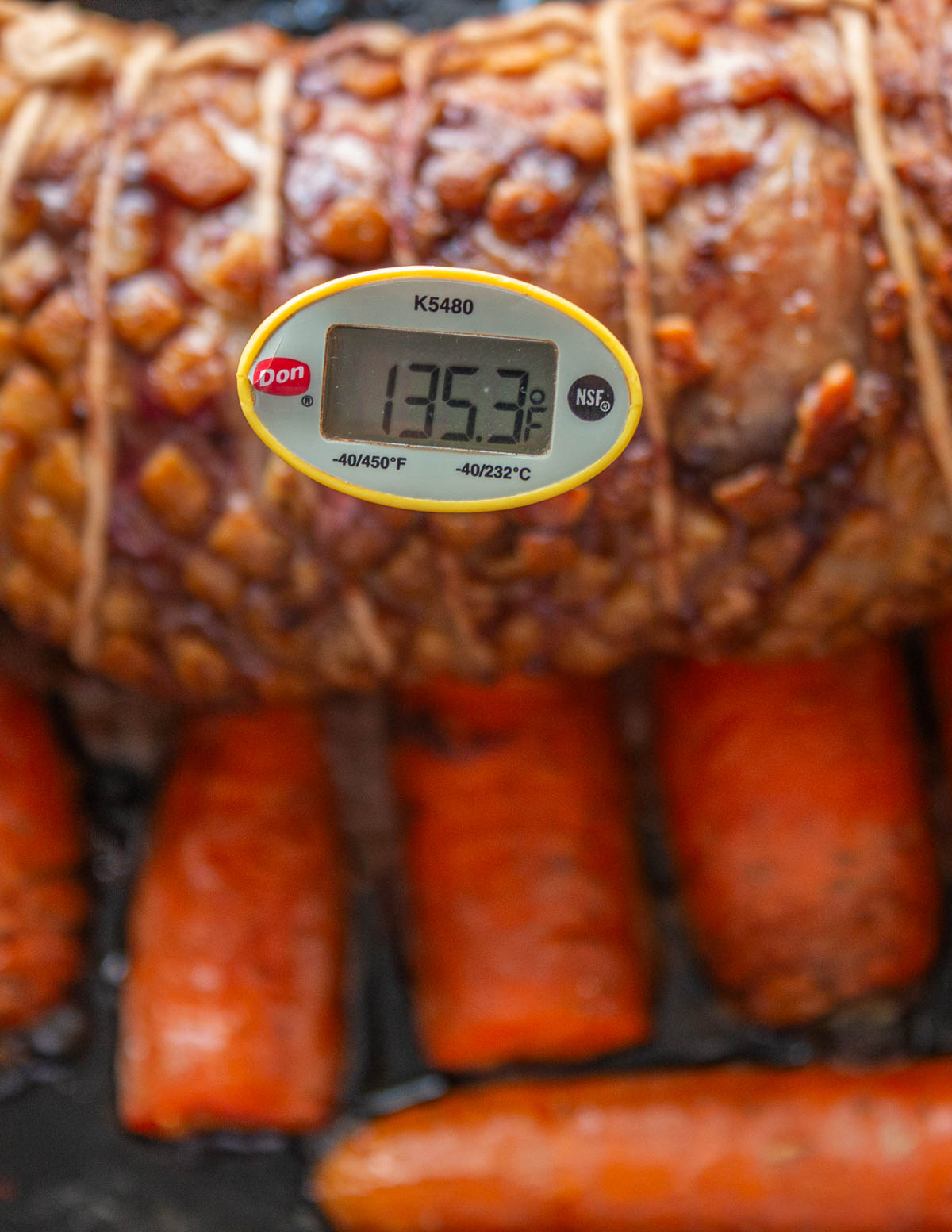 A thermometer sticking in a roasting lamb saddle showing 135 internal temperature.