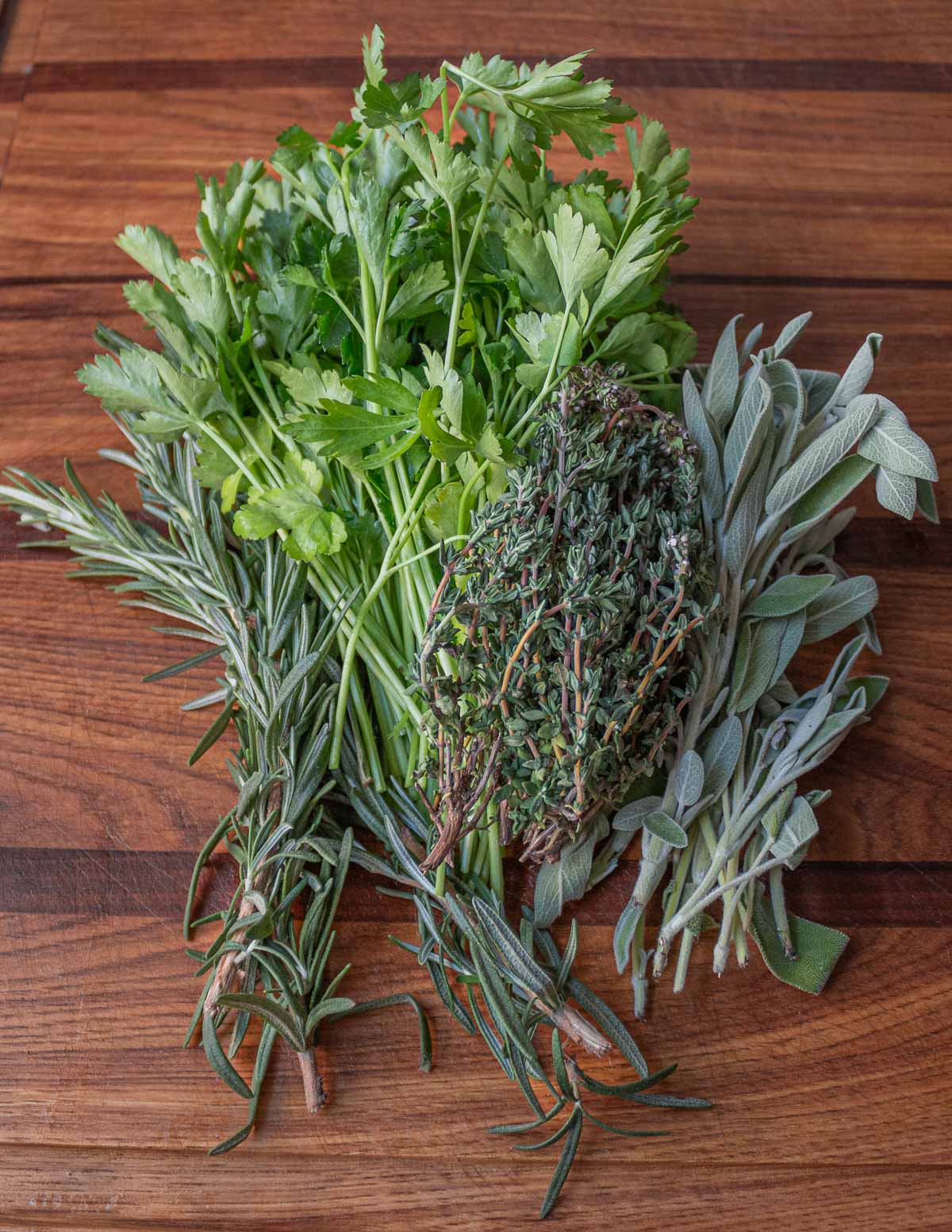 A mix of fresh parsley, rosemary, sage and thyme on a cutting board.