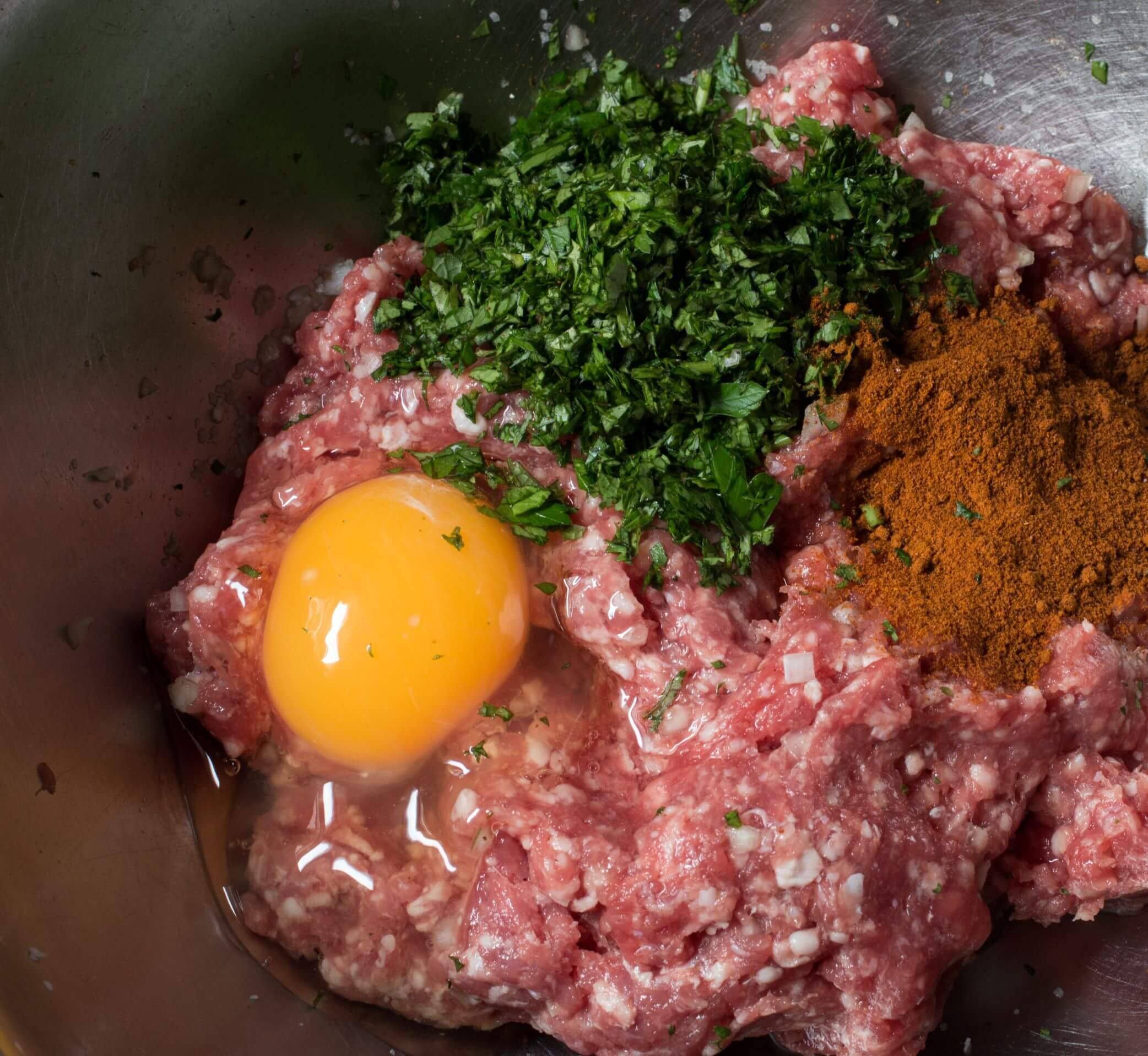 Mixing ground lamb with spices, herbs and egg in a mixing bowl.