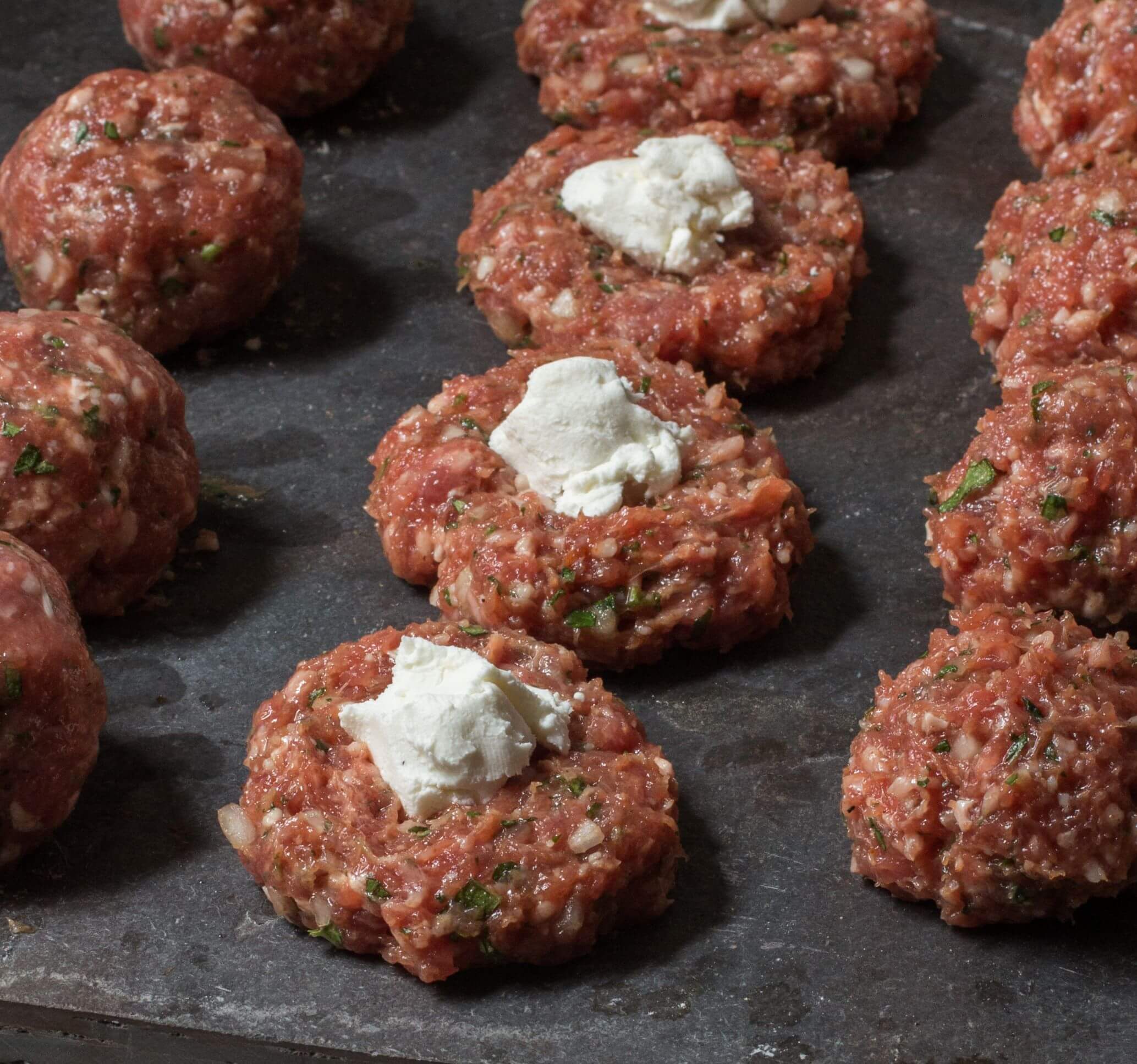 Forming ground lamb meatball mix around pieces of goat cheese on a board.