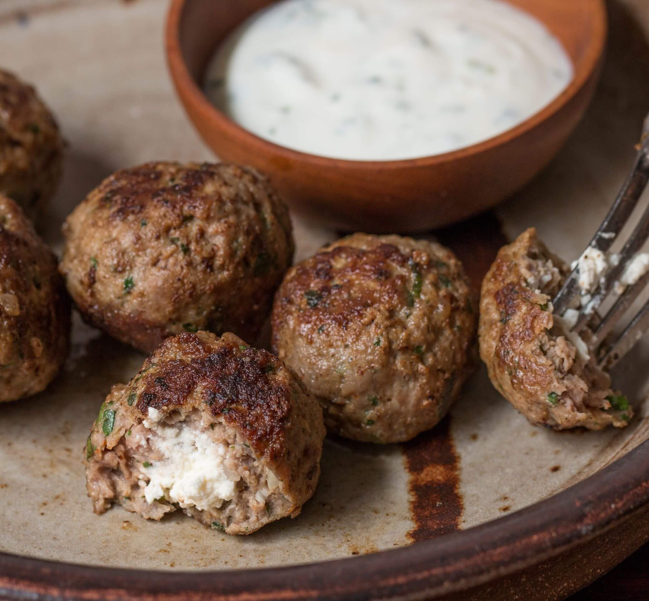 Cooked, stuffed lamb meatballs cut open to reveal the goat cheese stuffing inside.