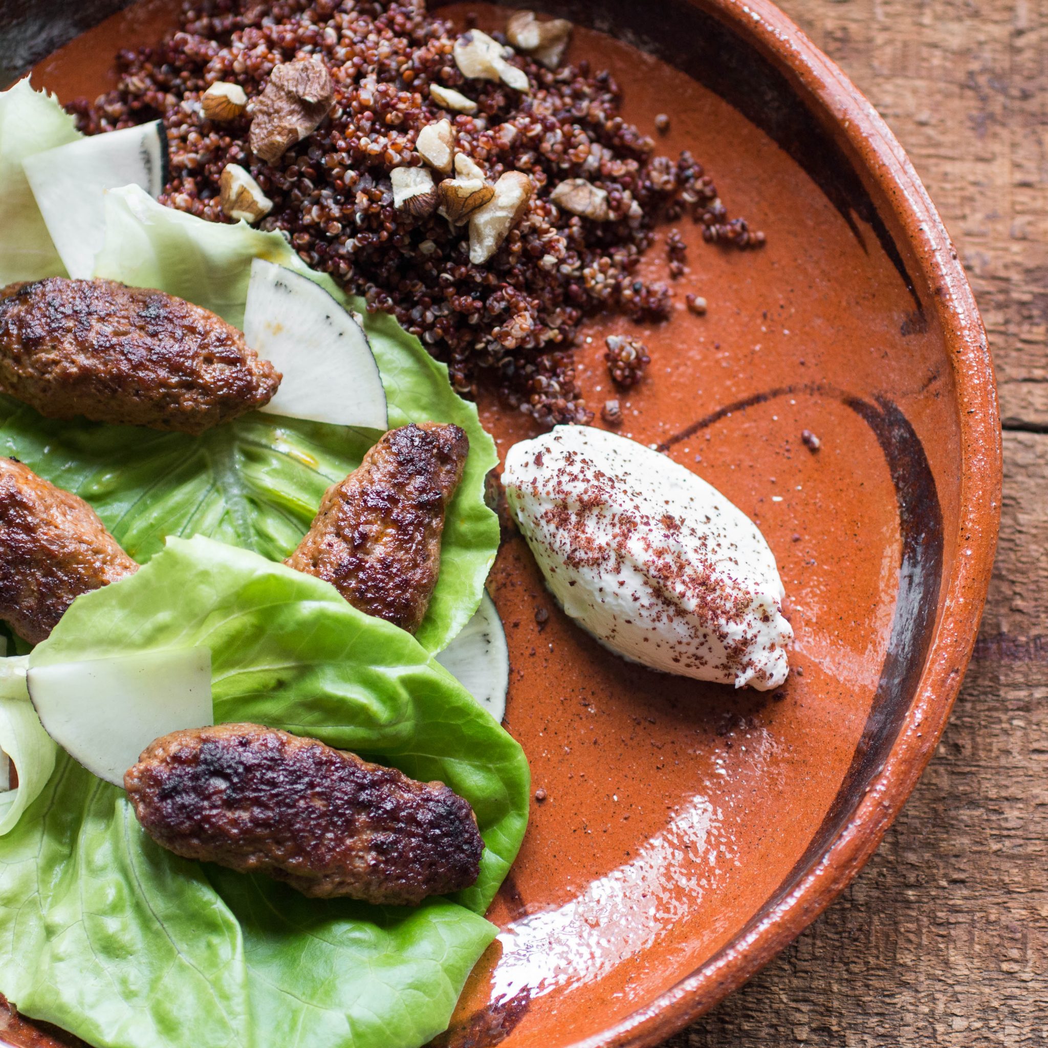 Cooked lamb merguez sausages on a plate with quinoa and lettuce. 