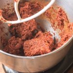 Mixing ground lamb meat with harissa paste in a stand mixer.