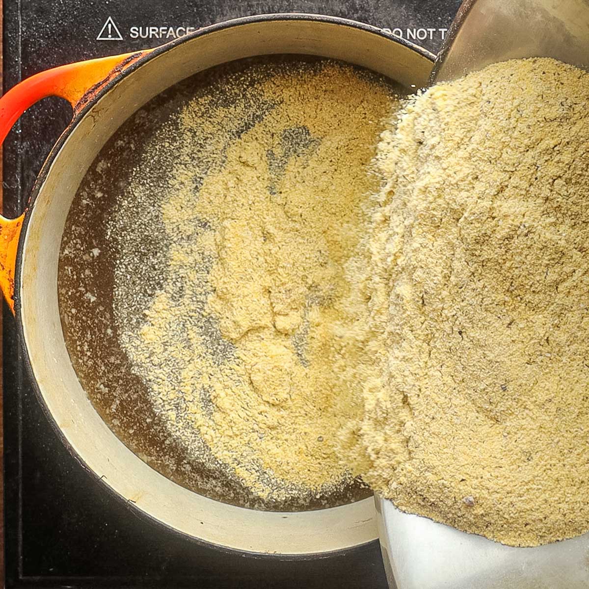 Adding cornmeal to meat stock in a Dutch Oven.
