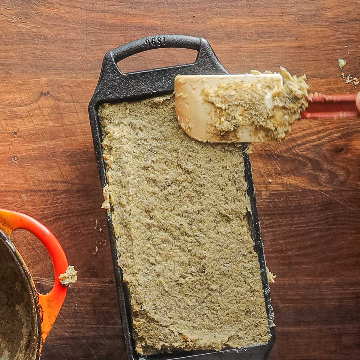 Putting cooked lamb scrapple into a loaf pan with a spatula.