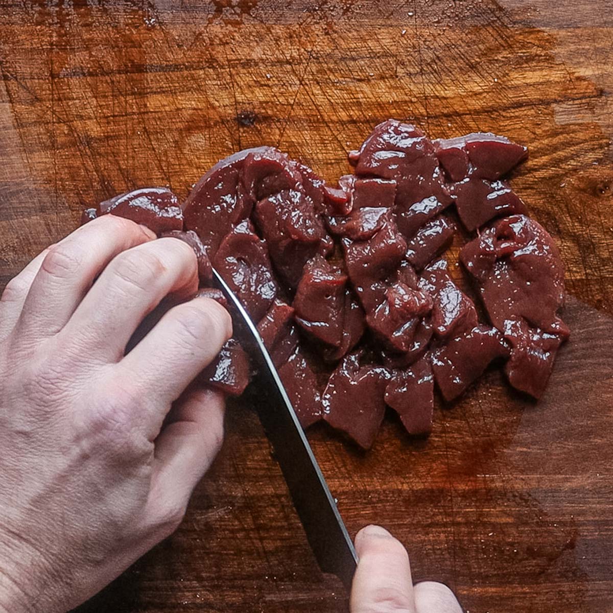 Dicing raw lamb liver on a cutting board.