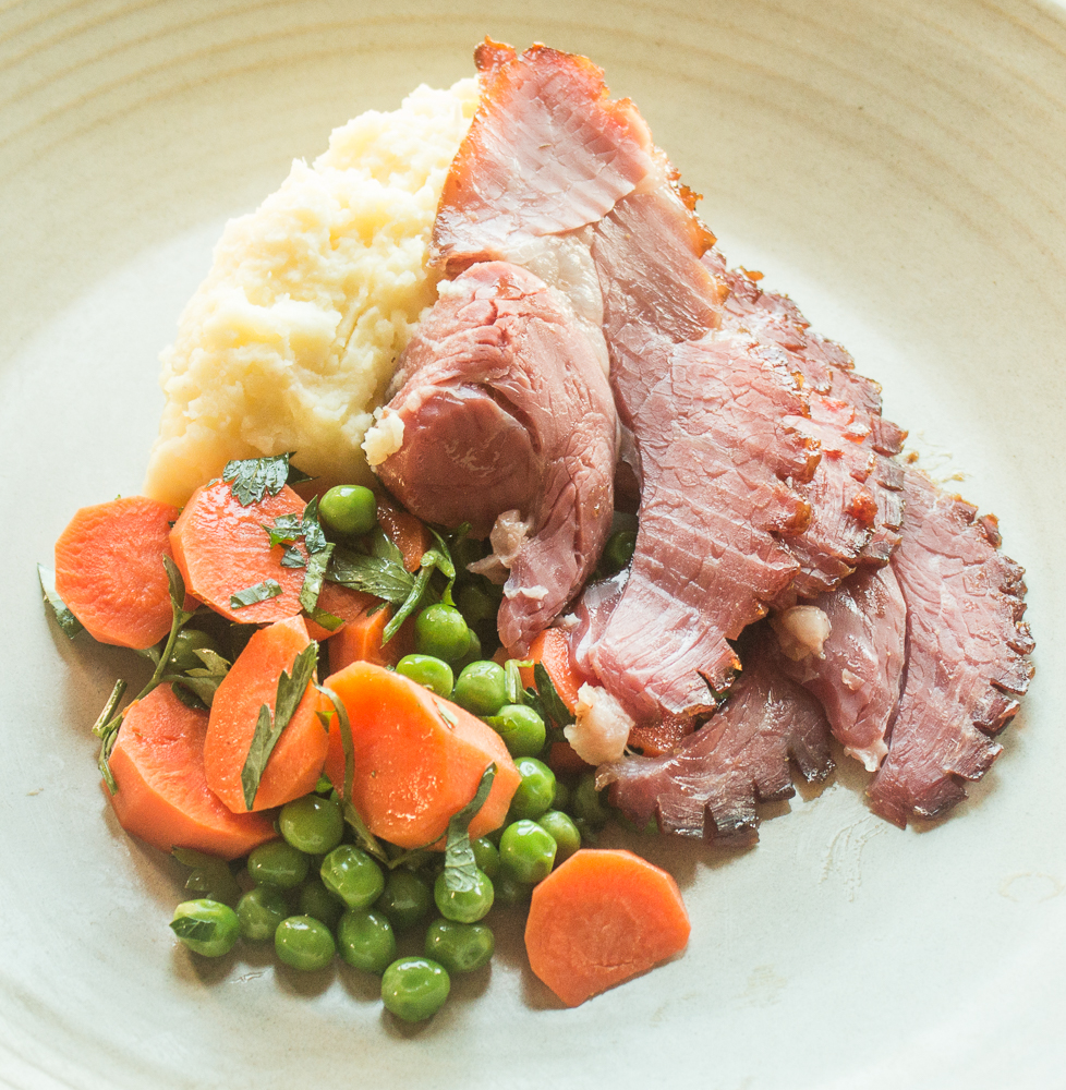 A plate of peas and carrots with mashed potatoes and slices of lamb ham.