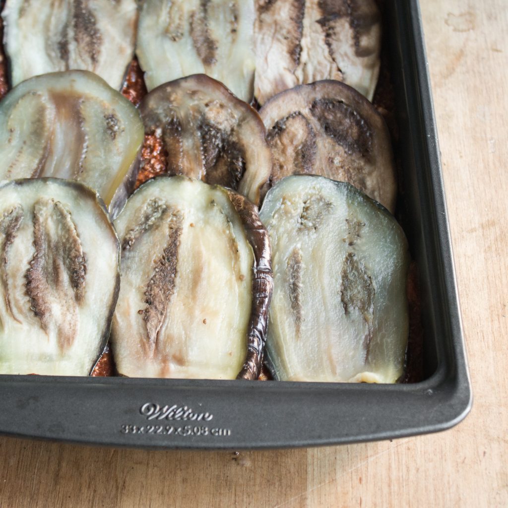 Laying eggplant slices in a pan lined with sauce to make musaka.