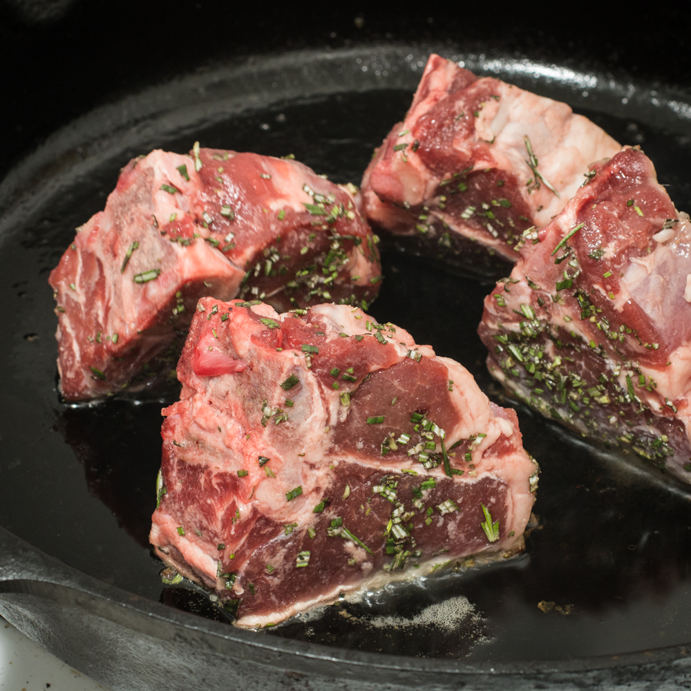 Searing rosemary lamb chops in a pan fat side down.