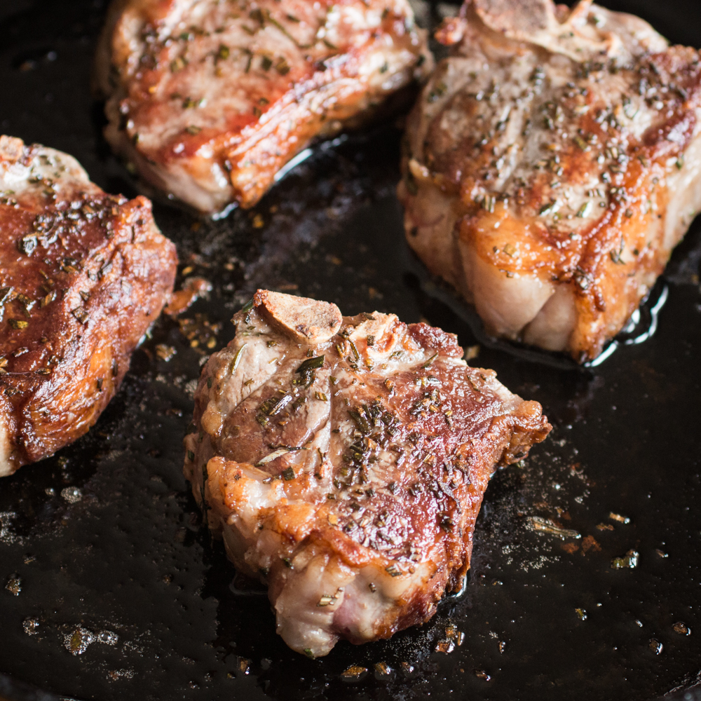 Golden brown seared rosemary lamb loin chops in a pan.
