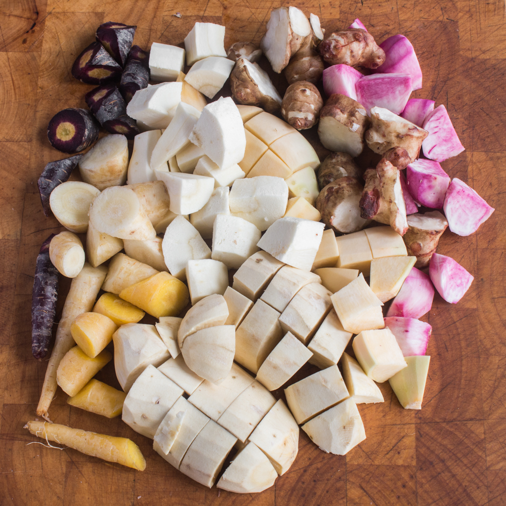 Differently colored root vegetables cut into pieces on a cutting board.