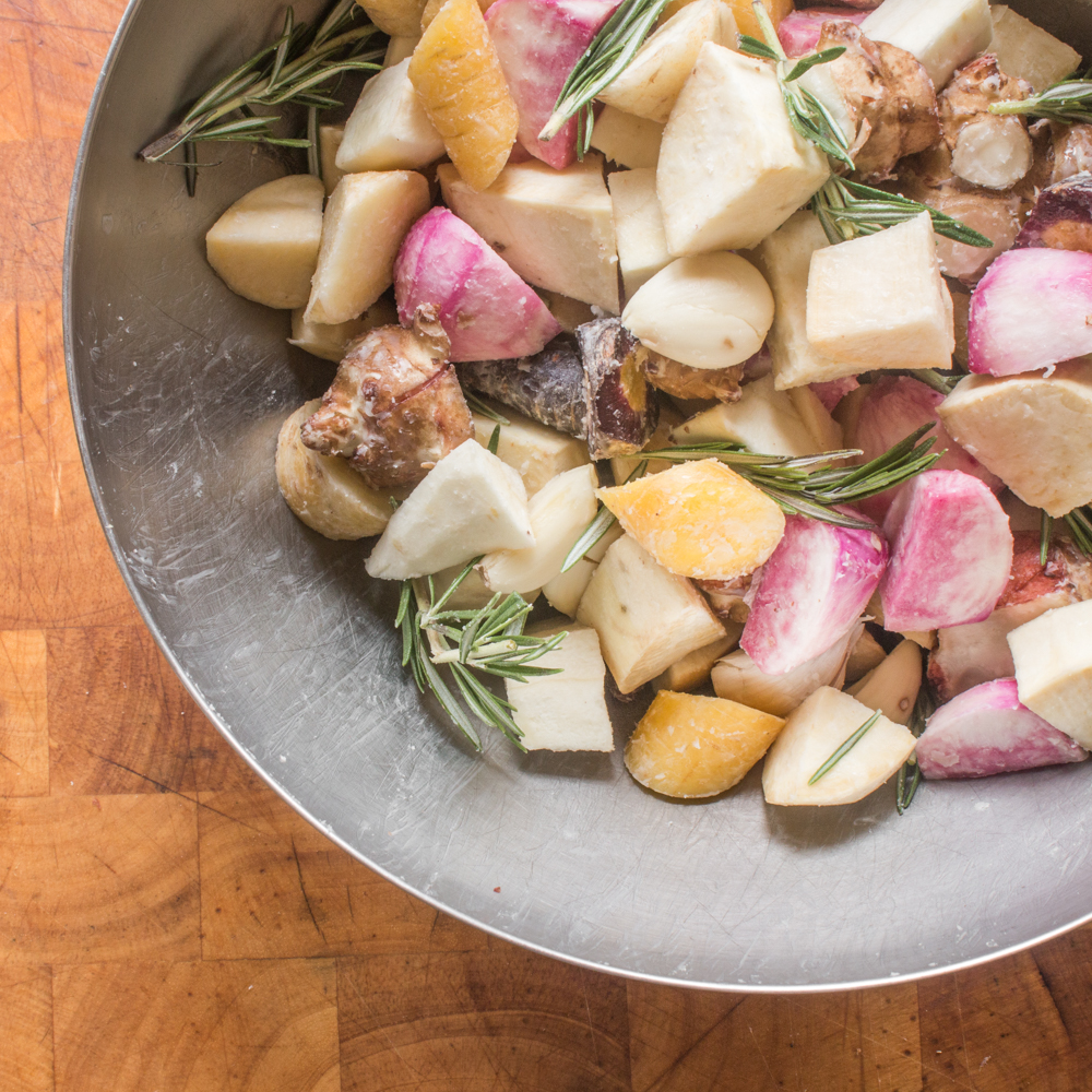 Diced root vegetables in a bowl seasoned with fat and rosemary.