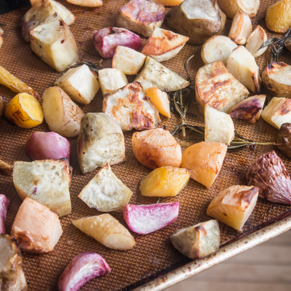 A baking sheet filled with roasted root vegetables as a side dish for lamb chops.