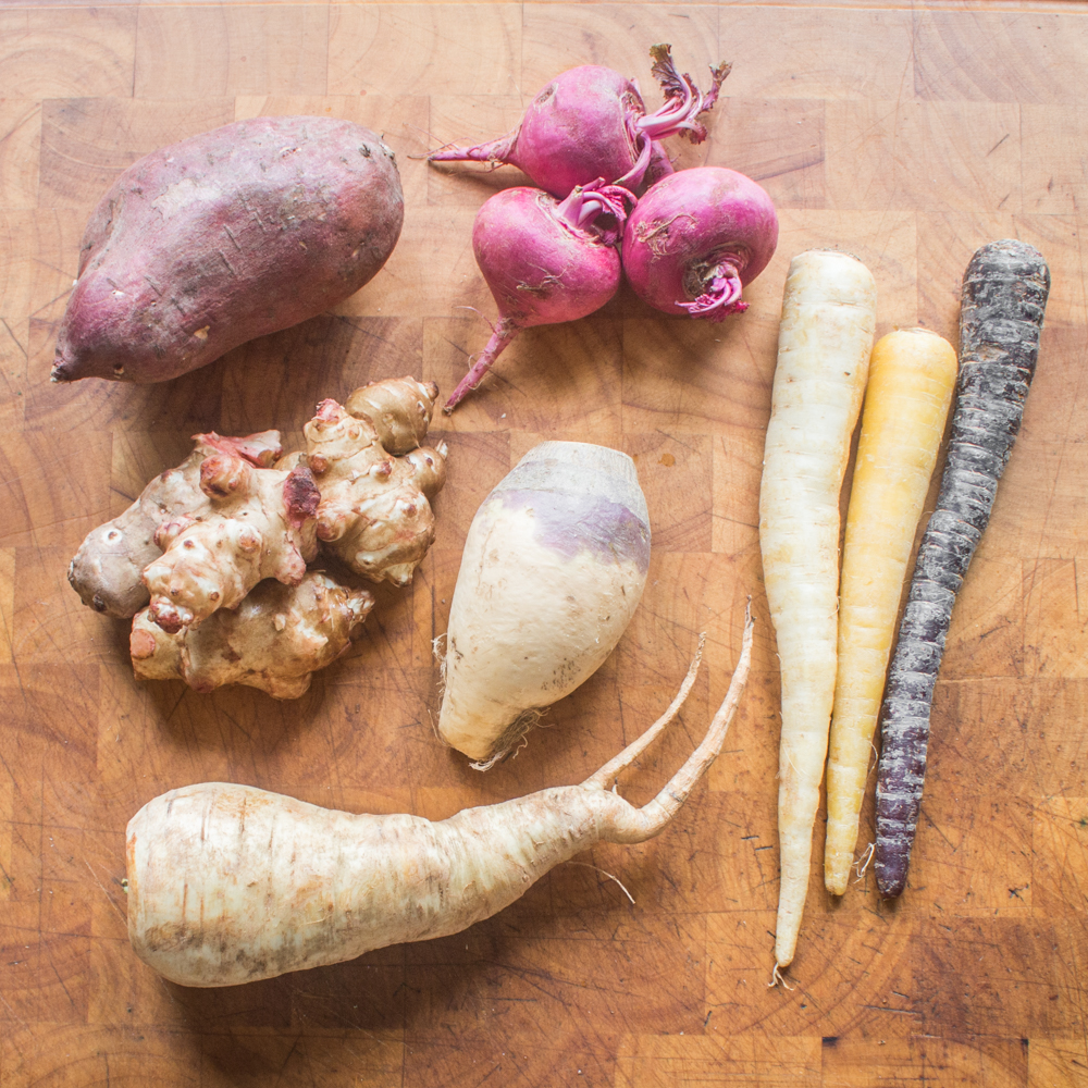 scarlet turnip, carrots, parsnip, sunchoke, lavender radish, rutabaga on a cutting board ready to be cleaned and roasted. 