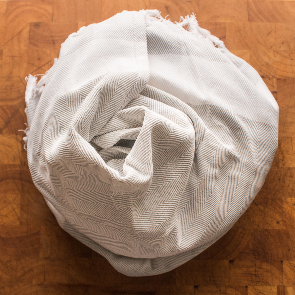 A Dutch oven filled with lamb plov wrapped in a towel cooling.