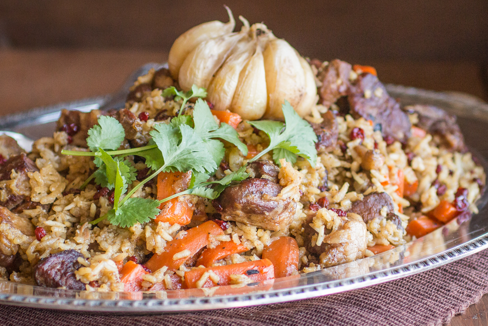 A plate of traditional lamb plov garnished with herbs and garlic bulb. 
