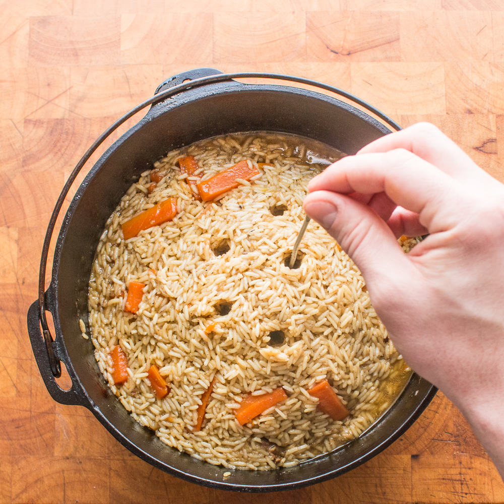 Poking holes with chopsticks in a Dutch oven filled with lamb plov to help the rice steam.