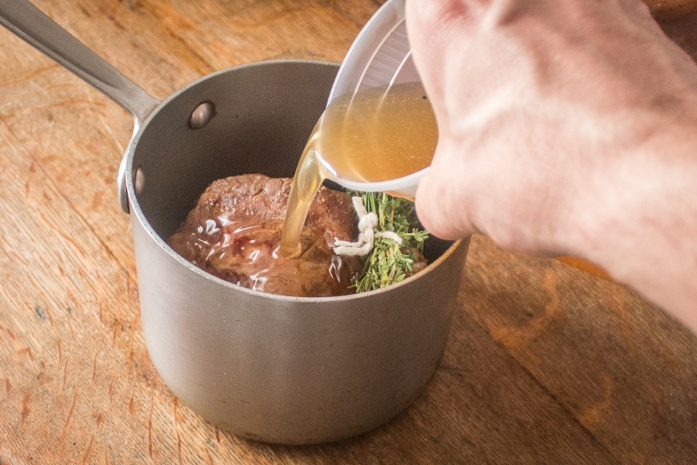 Pouring rendered lamb tallow over a lamb neck. 