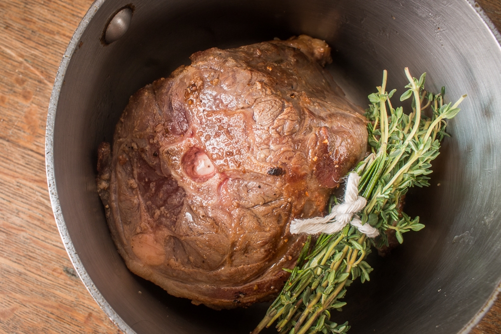 Lamb neck in a pot with herbs about to be made into confit. 