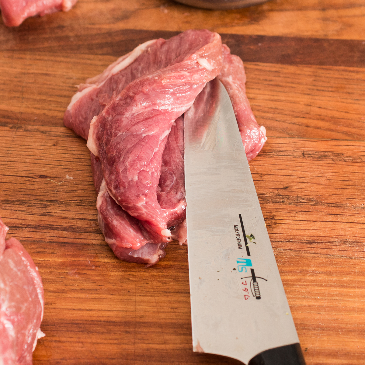 Cutting open a thick slice of lamb scallopini with a knife to butterfly it.