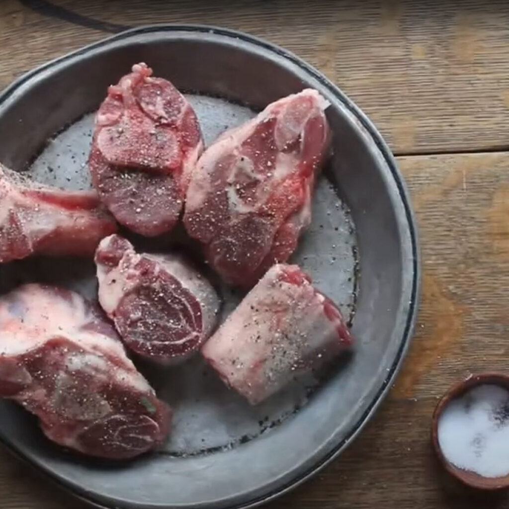 Seasoning lamb shanks with salt and pepper.