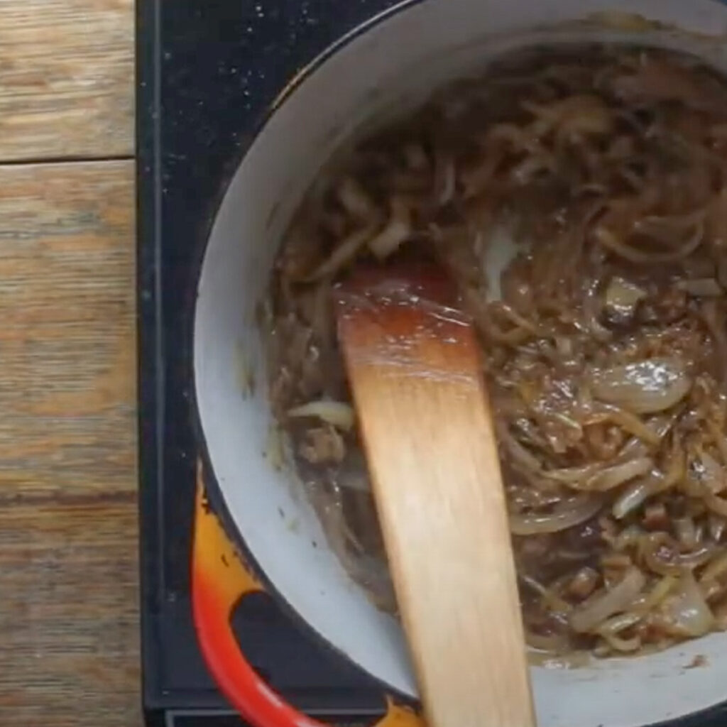 Stirring a pot of caramelized onions with a wooden spatula.