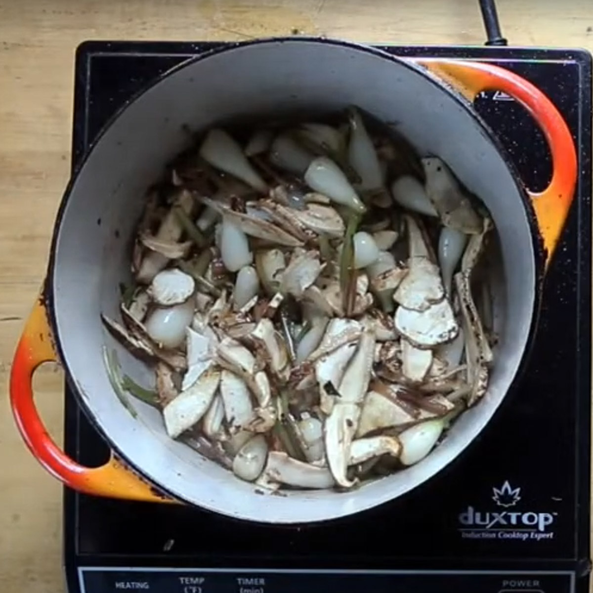 Adding mushrooms to a pot of spring onions for soup.