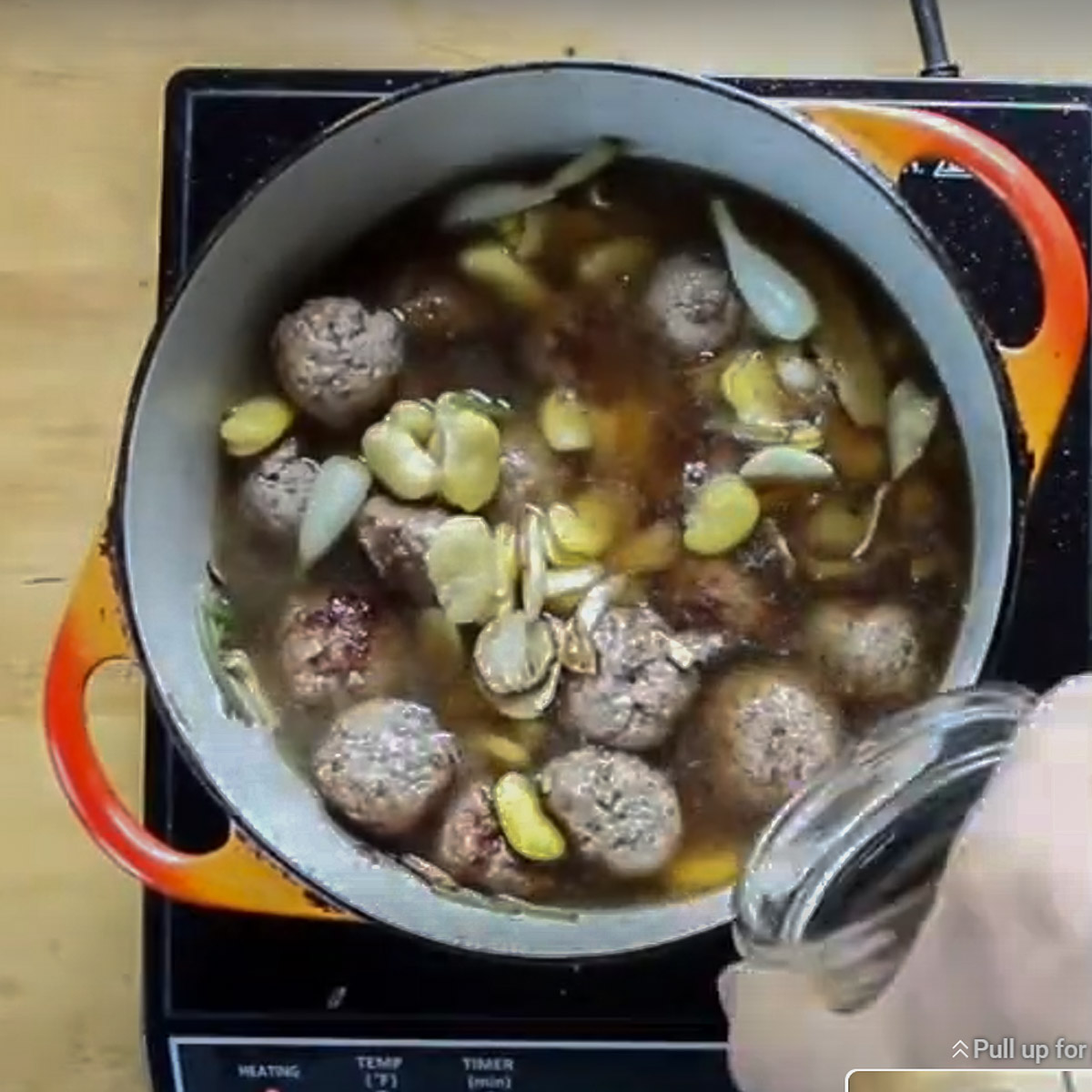 Adding stock to a pot of lamb meatball soup.