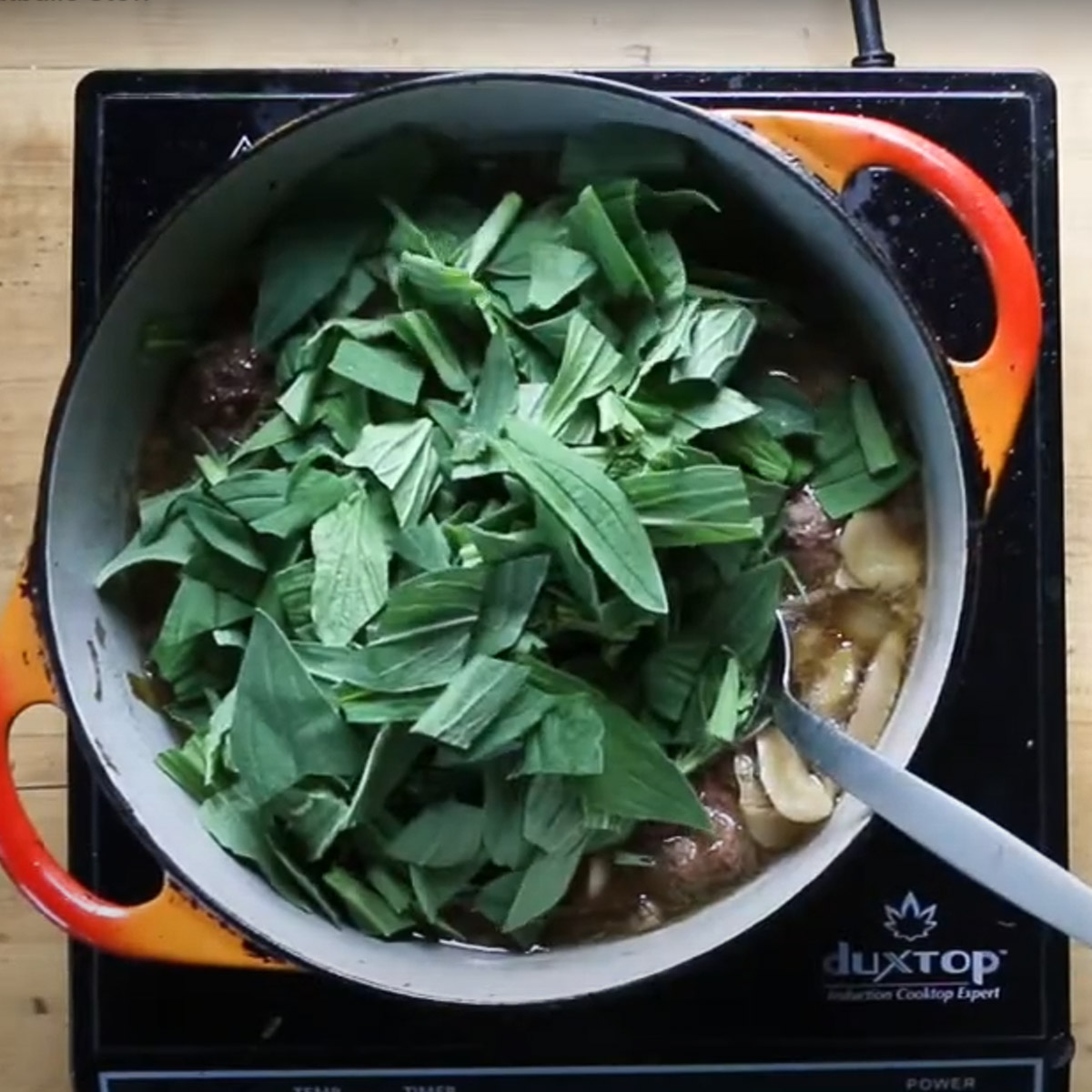 Adding chopped greens to a pot of lamb soup.