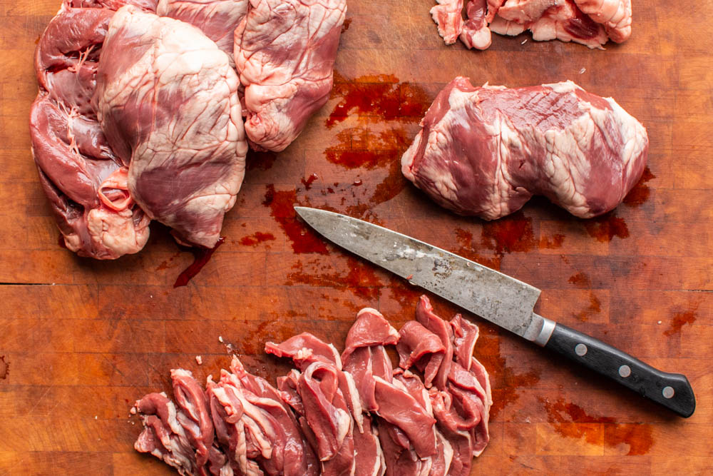 Thinly slicing lamb and goat hearts on a wooden block with a japanese knife