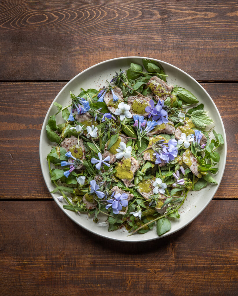 Goat tongue salad with salsa verde, fresh greens and wildflowers on a plate. 