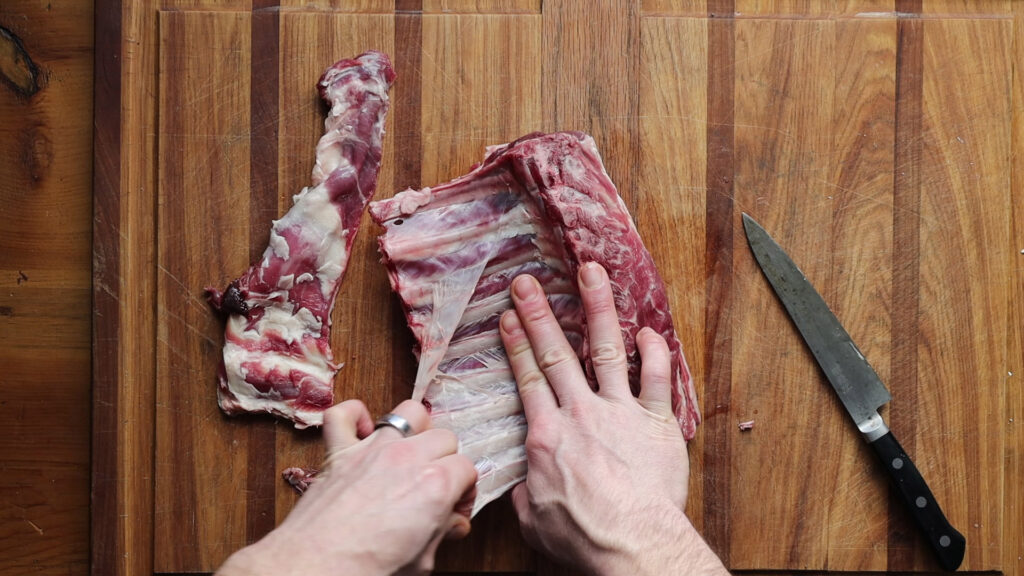 Using fingers to remove the silverskin from a rack of lamb.