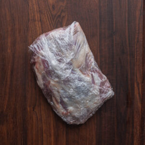 A lamb shoulder seasoned and wrapped in plastic.