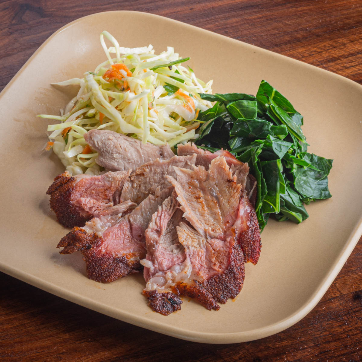 A sliced smoked lamb shoulder on a plate with colseslaw and cooked greens.