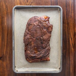 A smoked lamb shoulder on a baking sheet lined with parchment.