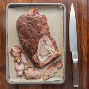 A smoked lamb shoulder being sliced resting on a baking sheet with parchment.