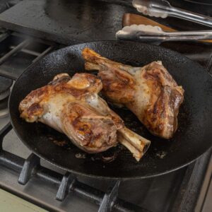 Browning lamb shanks in a carbon steel pan.