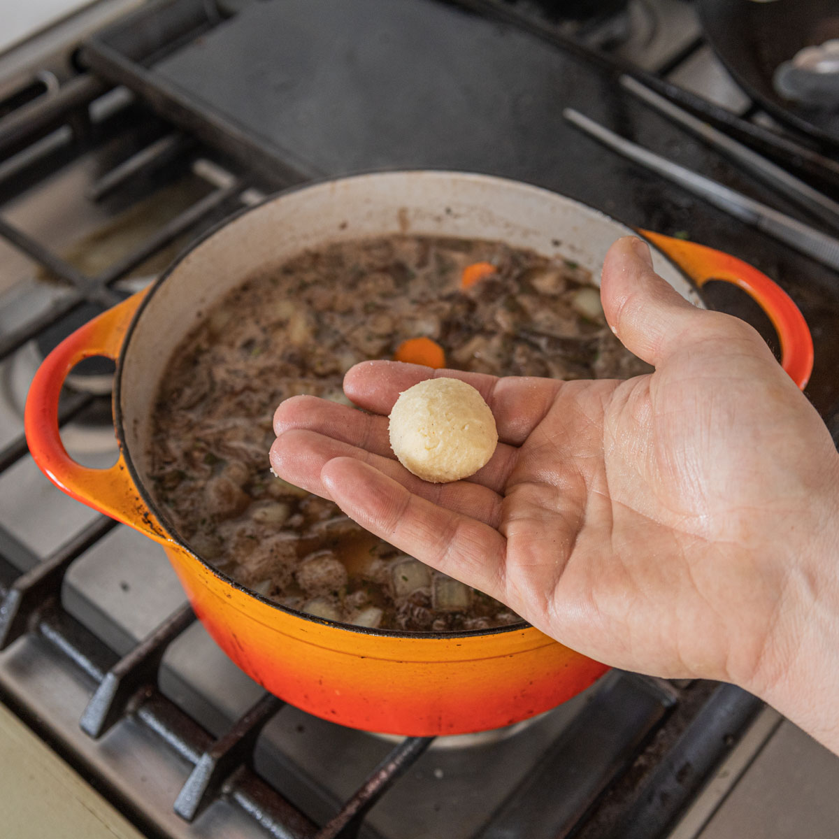 A hand adding a ball of kneaded roux to a pot of stew.