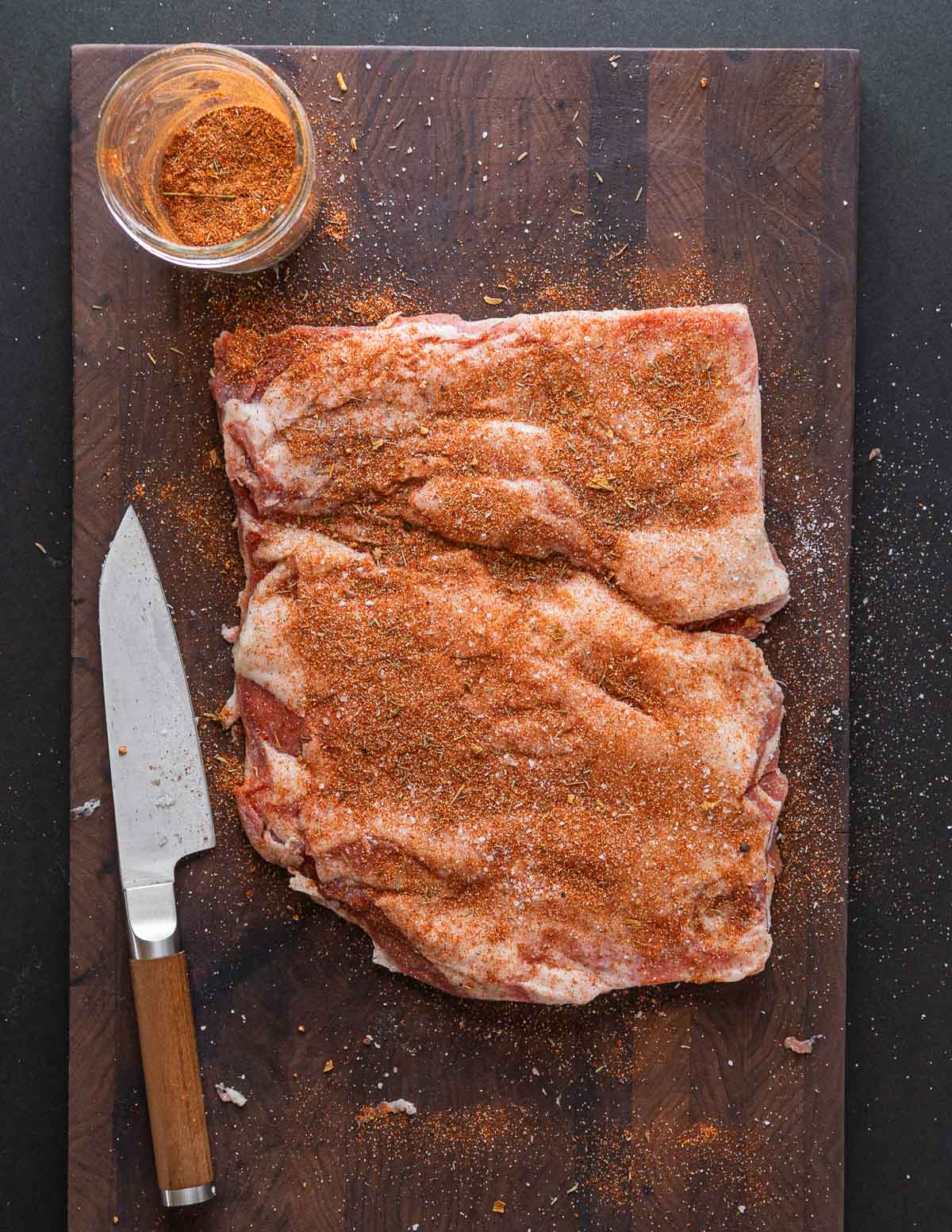 Seasoning both sides of a trimmed lamb breast.