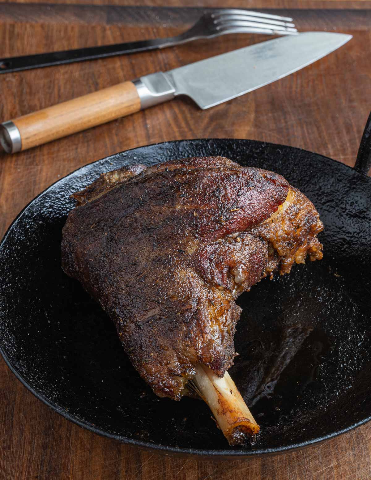 A smoked lamb shank in a kehoe carbon steel pan with a knife in the background.