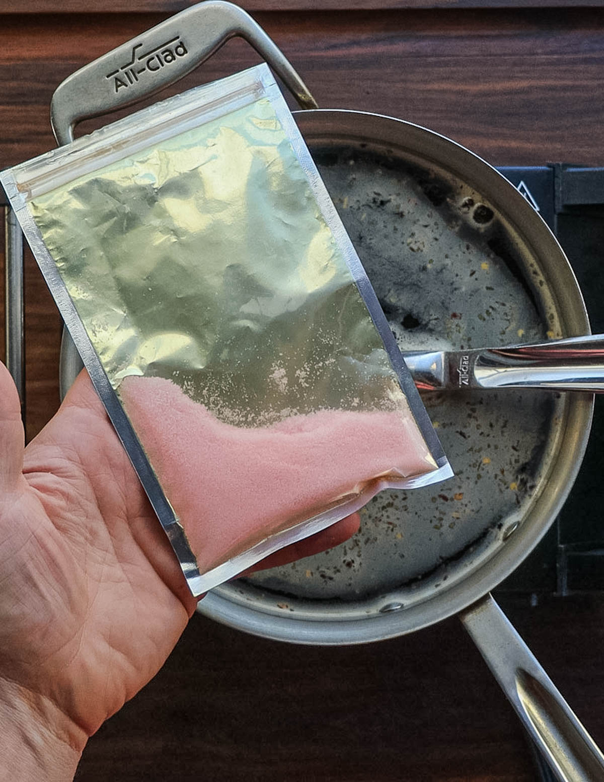 A hand holding a bag of pink curing salt or instacure number 1.