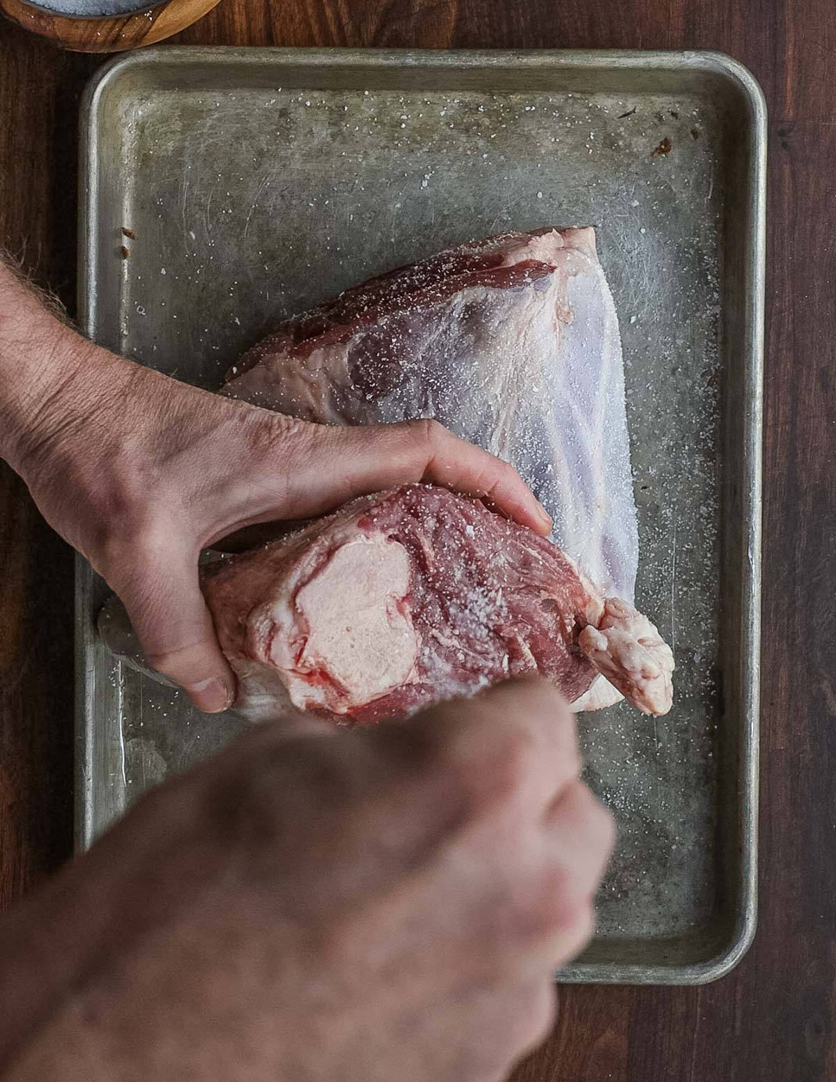 Seasoning a lamb shank with salt before smoking.