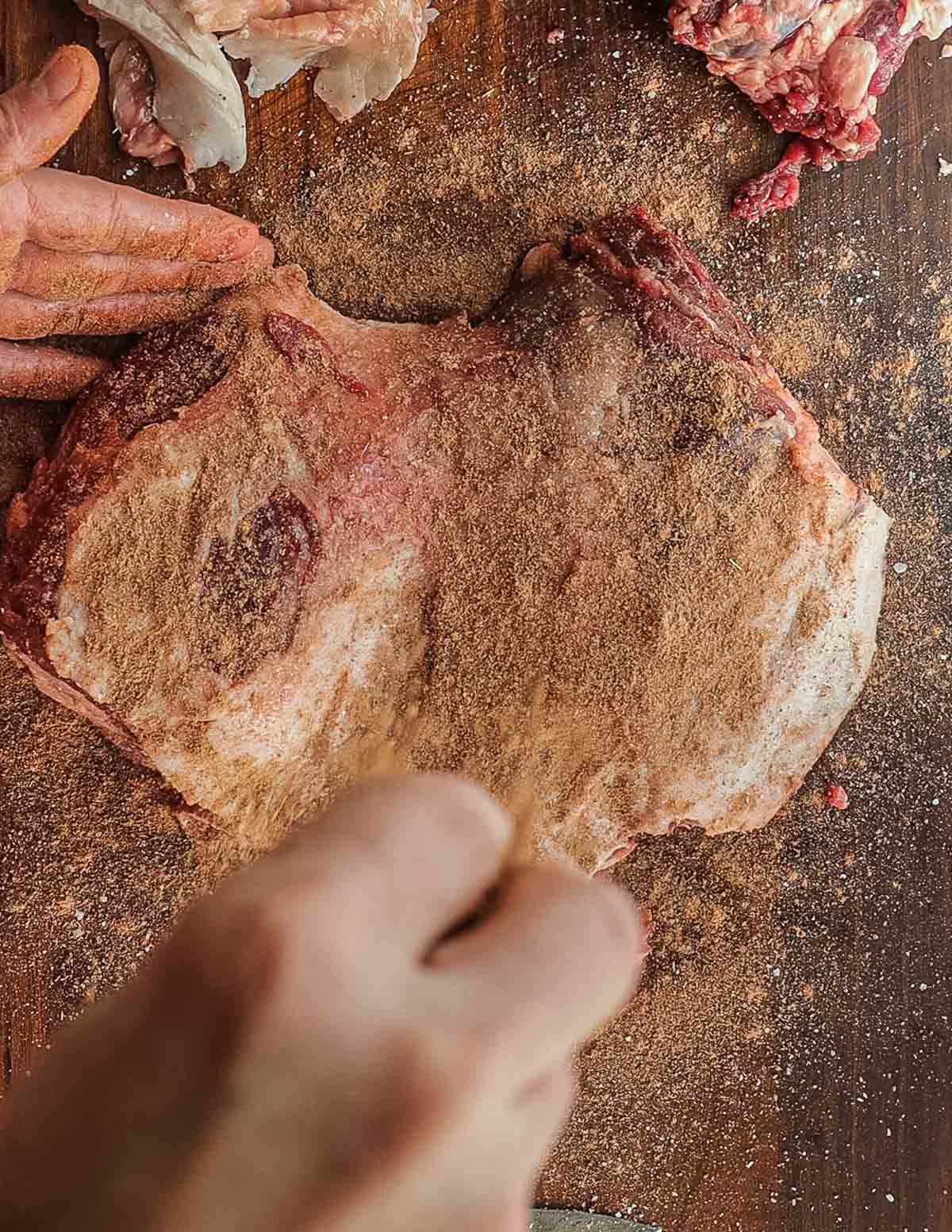 Seasoning a boneless leg of lamb with a dry rub spice blend.