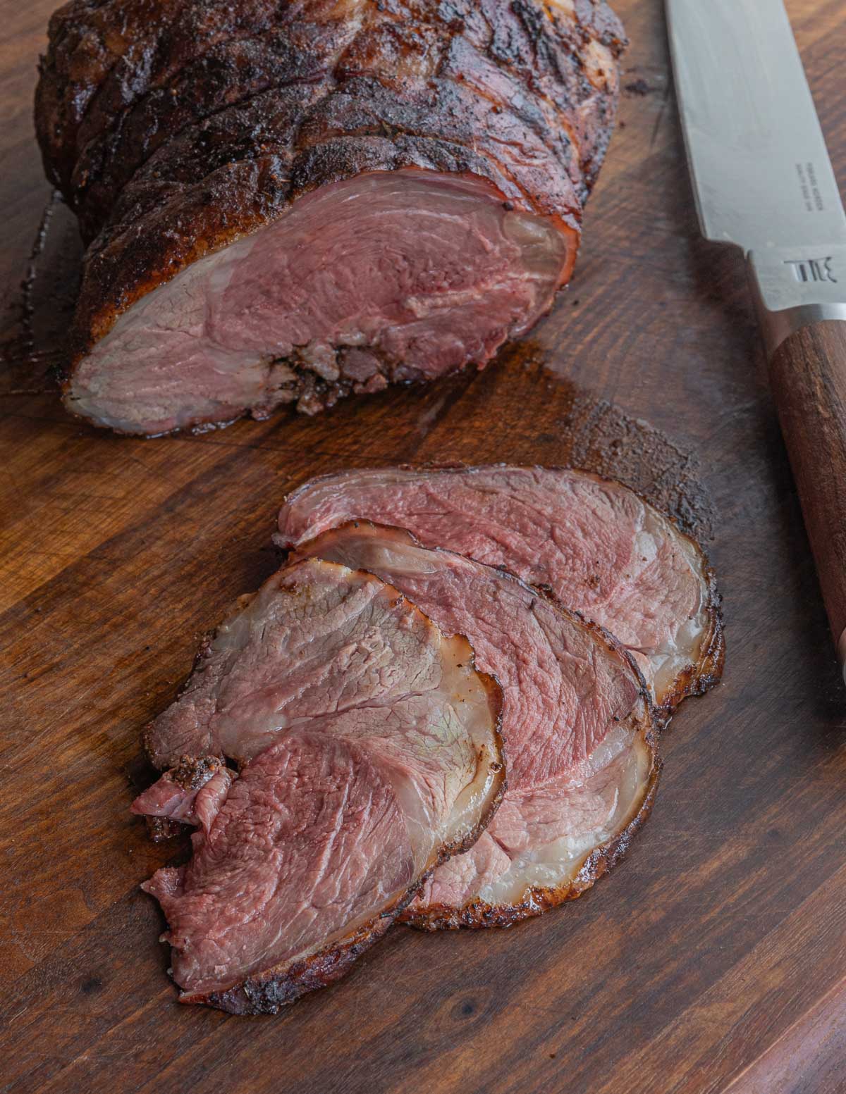 A sliced, smoked leg of lamb next to a knife on a cutting board.